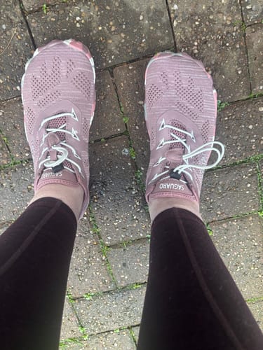 A reviewer's feet in mauve Smart II Barefoot Shoes with white laces, standing on a paved walkway.