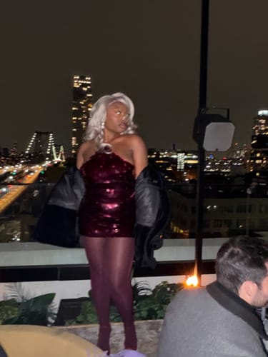 Customer on a rooftop at night wearing the cherry sequin Open Back Halter Top with a jacket.