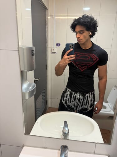 Customer in a restroom mirror selfie, showing the fit of a black compression shirt and shorts.