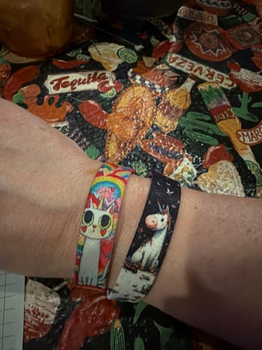 Reviewer wearing two colorful Sparkle on Bracelets on their wrist, one with a caticorn design and another with a unicorn.