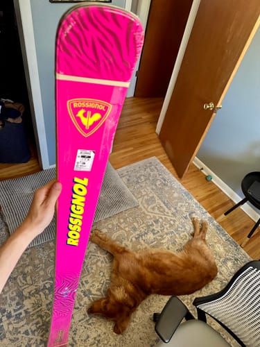 Reviewer holding a bright pink Rossignol Super Arcade Ski with a patterned tip and yellow lettering.