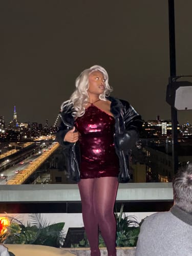 Customer on a rooftop holding a jacket, showing the front of the cherry Sequin Open Back Halter Top.