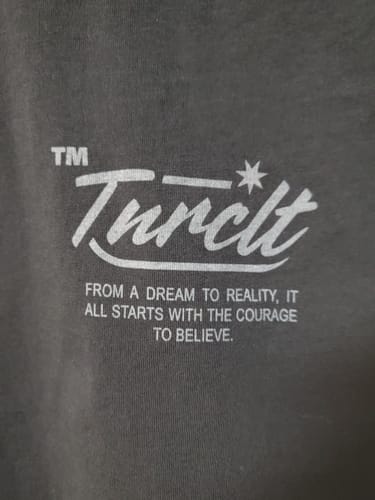 Close-up of a reviewer's dark grey MYSTERY TEE with its white 'Tunclt' logo and motivational text.