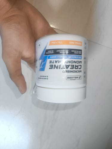 A reviewer's hand holding the white tub of Wellcore Micronised Creatine Monohydrate.