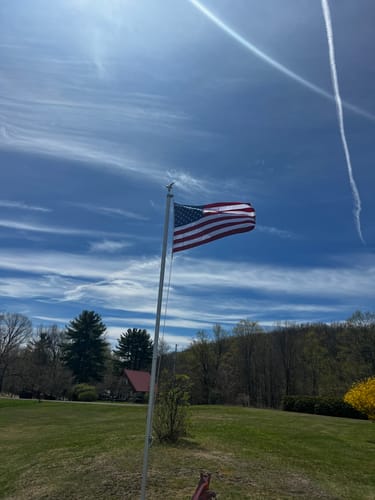 Customer's Heavy Duty American Nylon Flag waving on a tall flagpole in a yard under a blue sky.