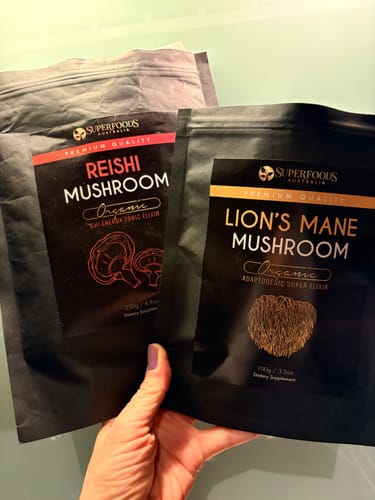 Customer's hand holding a pouch of Lion's Mane Mushroom Extract alongside a pouch of Reishi Mushroom.