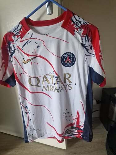 Client montrant son maillot spécial PSG blanc avec des motifs rouges et bleus, accroché à un cintre.