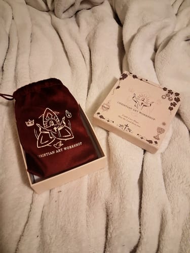 Customer's branded box and burgundy velvet pouch for the rosary on a white blanket.