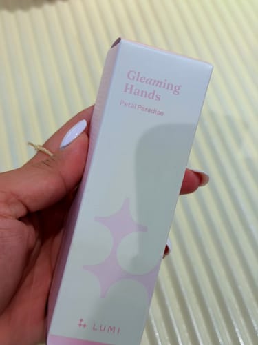 Reviewer holding the white and pink box for Gleaming Hands Petal Paradise hand cream.