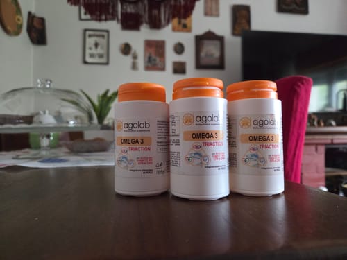 Cliente mostra tre flaconi bianchi di Omega 3 su un tavolo in un ambiente domestico.