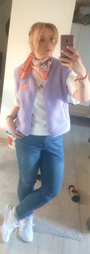 Kundin trägt die lila Teddyweste über einem weißen T-Shirt mit Jeans und einem orangefarbenen Schal.
