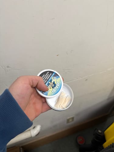 Customer holding an open round tin of Drifters Blueberry Lemonade Ice Nicotine Pouches with several pouches visible inside.