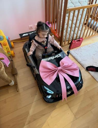 Avaliação de cliente de uma criança sentada no carro elétrico MERCEDES GT3 preto com um grande laço cor-de-rosa no capô.