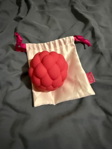 Customer's red Berri massager shown with its white satin storage bag on a dark sheet.