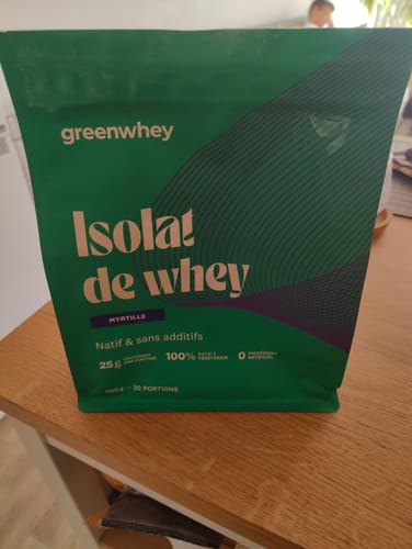 Photo d'un client du sachet vert d'Isolat de Whey Native, saveur myrtille, posé sur une table.
