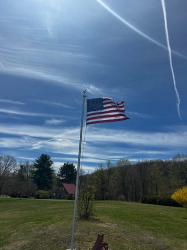 Customer's Heavy Duty American Nylon Flag waving on a tall flagpole in a yard under a blue sky.
