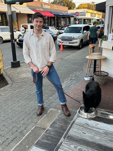 Customer wearing brown Tankwa Boots with cuffed blue jeans while standing on a city sidewalk with a dog.
