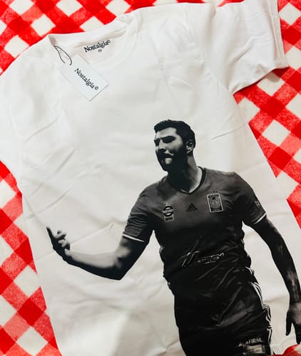 Un cliente muestra la camiseta Gignac blanca con un estampado en blanco y negro, sobre una superficie a cuadros.
