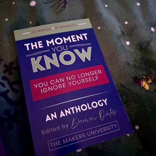 Reviewer's copy of 'The Moment You Know' book resting on a green patterned blanket.