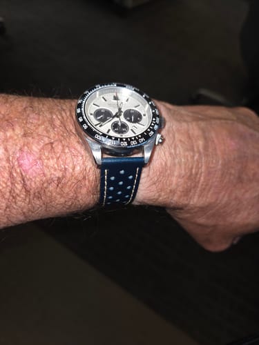 A person's wrist wearing a watch with the blue perforated Leather Sport Grip strap and tan stitching.