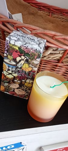 Customer's Gilded Ylang Fragrance Oil packaging next to a finished yellow candle in a frosted glass.