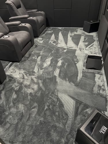 Customer's plush charcoal Mellow Mat on the floor of a dark home theater room, next to two recliner chairs.