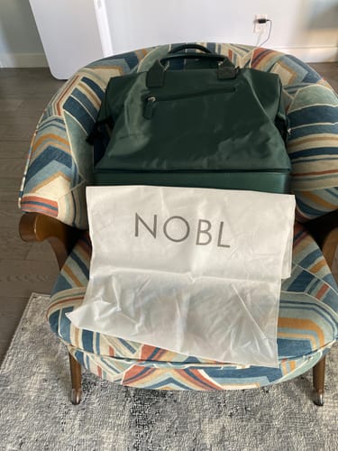 Customer's white Weekender Dust Cover displayed with the green Weekender bag on a patterned chair.