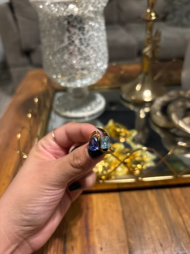 Close-up of a customer's hand holding the Navae Birthstone Ring with its gold band, a purple and a light blue stone.