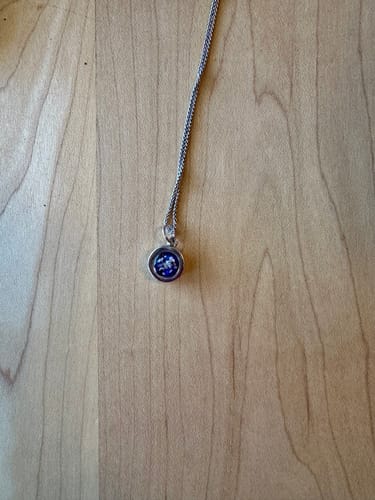 Customer's dainty silver circle cremation ash pendant with purple and blue opal inlay, on a wood surface.