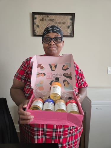 Customer holding an open pink box displaying five bottles of Skin Smoothing Body Oil.
