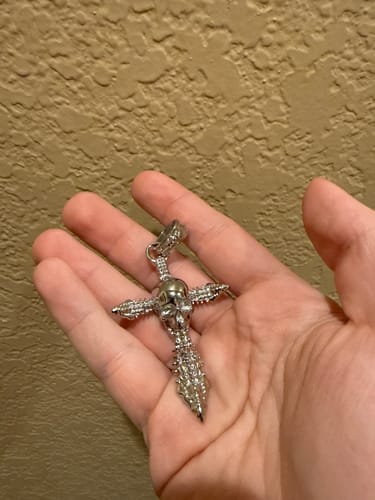 Reviewer holding the detailed, silver exclusive jewelry piece in their palm, showing its skull and dagger design.