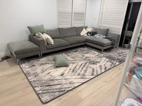 Customer's Mellow Mat v2 Designer Print rug placed in front of a large grey sofa in a living room.