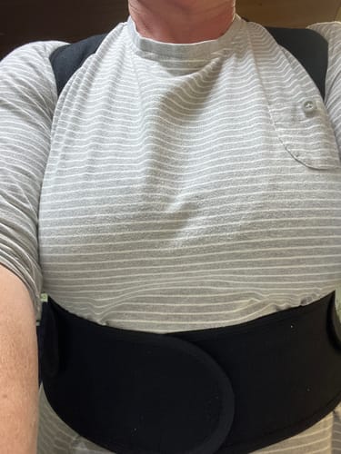 Vásárló egy csíkos póló felett viseli a fekete Ergonomikus Tartásjavító Hevedert.