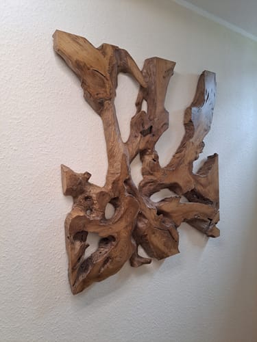 Kunde zeigt das einzigartige Wandbild NAGA aus Teakholz, das an einer strukturierten weißen Wand hängt.