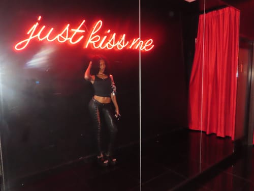 Reviewer wearing the black low-rise Vice Pant while posing in a dark room with a red neon sign.