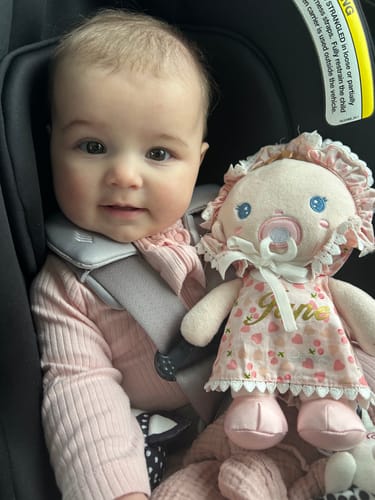 Reviewer's baby sits in a car seat next to the soft Personalized Cherry Baby Girl doll.