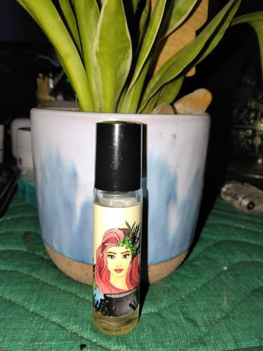 Customer's Garden Witch roll-on perfume bottle with a colorful label, in front of a potted plant.