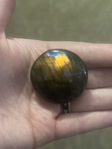 Customer holding a dark, polished crystal from their VIP Crystal Club subscription in their hand, showing a yellow and blue flash.