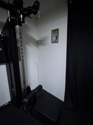 Kunde zeigt den schwarzen Latzug Sitz, der stabil in einer Ecke an einer Kraftstation montiert ist.