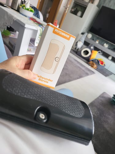 Ein Rezensent hält die Verpackung der Fellwunder Bürste, während die schwarze Bürste im Vordergrund liegt.