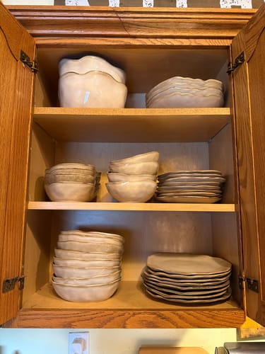 Reviewer's Crema stoneware plates and bowls from the set stacked in a wooden cabinet.