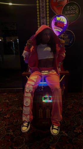 Reviewer in an arcade wearing the pink SEEK VISIONZ SET, which includes a zip hoodie and matching pants.