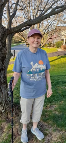 A reviewer smiles while wearing the blue Out Of Breath T-shirt outdoors with a walking pole.