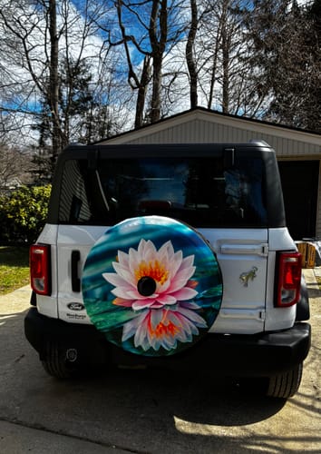 Customer's Pink Water Lily Print Tire Cover with camera hole shown fitted on the spare tire of a white vehicle.