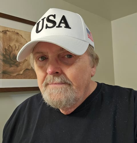 Reviewer wearing the white USA 250th Anniversary Hat, showing the black embroidered 'USA' on the front and flag patch on the side.