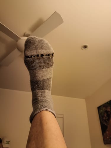 Reviewer wearing grey Quarter Socks with a dark grey band, holding their foot up.