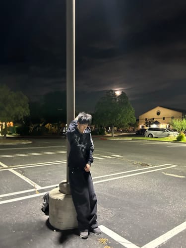 Customer wearing the black TLV ZIPUP while leaning against a pole in a parking lot at night.