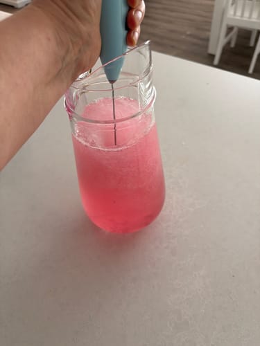 Customer using their light blue Electric Mixer to stir a fizzy pink drink in a glass pitcher.