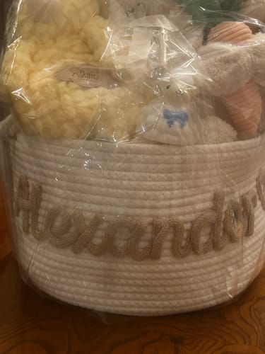 Customer's white personalized knitted basket with the name "Alexander" in beige yarn, filled with gifts and wrapped.