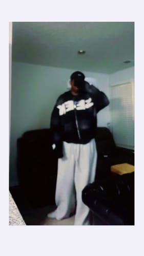 Reviewer standing indoors wearing the black SEEK ZIPUP hoodie, showing its bold front lettering.